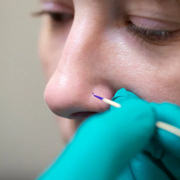 hand in a medical glove making a marking on the nose for a nostril piercing at IRIS Studios in Boulder Colorado