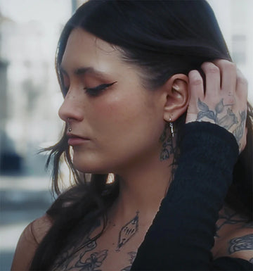 woman pulling her hair back behind her ear to show her earlobe piercing she got at IRIS Studio